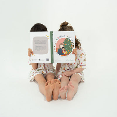 Two children sitting on the floor holding a Children's Christmas book with a white background