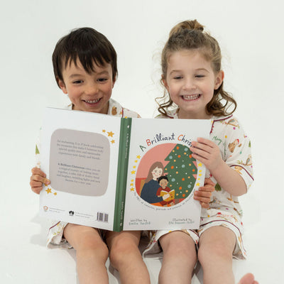 Two children holding a book titled 'A Brilliant Christmas' on a white background