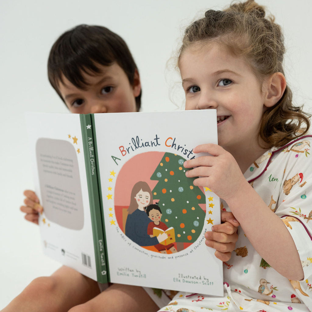 Two children holding a book titled 'A Brilliant Christmas' with a Christmas tree illustration on the cover.