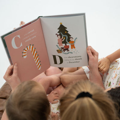 Children reading a book together with a focus on the cover featuring Christmas-themed illustrations.
