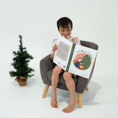 Child sitting in a chair reading a book with a small Christmas tree in the background