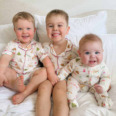 Three children in christmas pyjamas sitting on a bed.