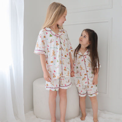 Two children in matching christmas pajama sets standing on a white surface with a white wall background.