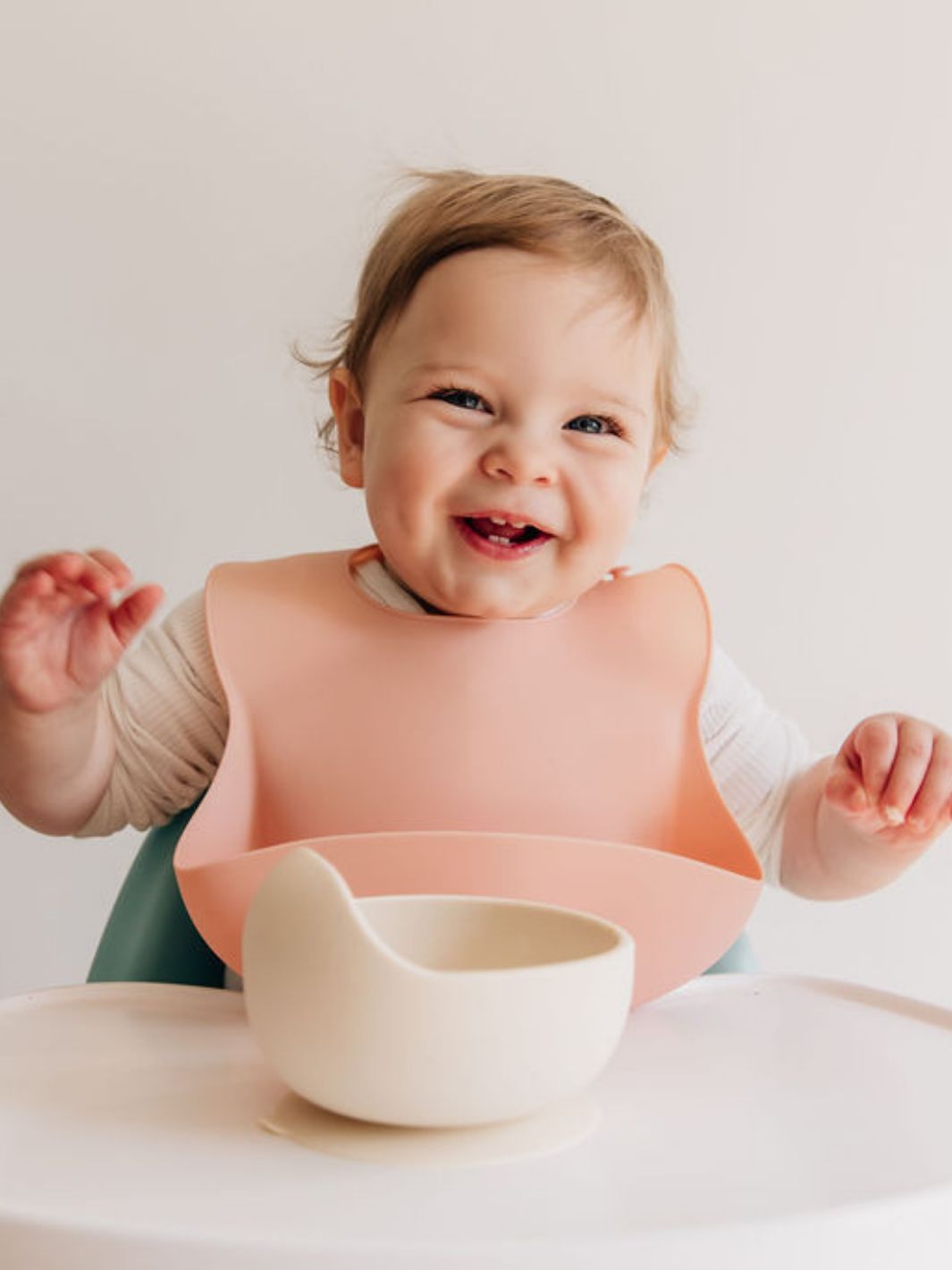 Happy baby wearing dusty rose silicone baby bib with suction bowl on high table